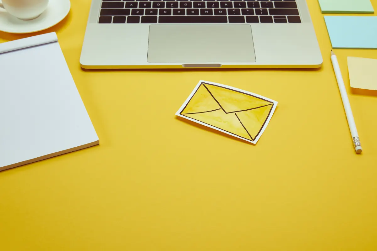 laptop on a yellow table and a yellow email envelope.