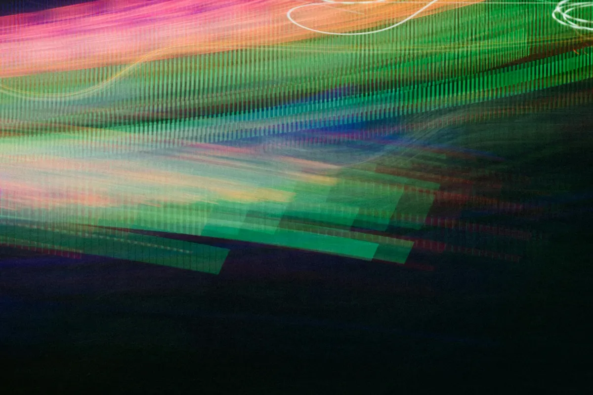 Abstract blurred motion of vibrant green, pink, and blue light streaks conveying speed and movement on a dark background.