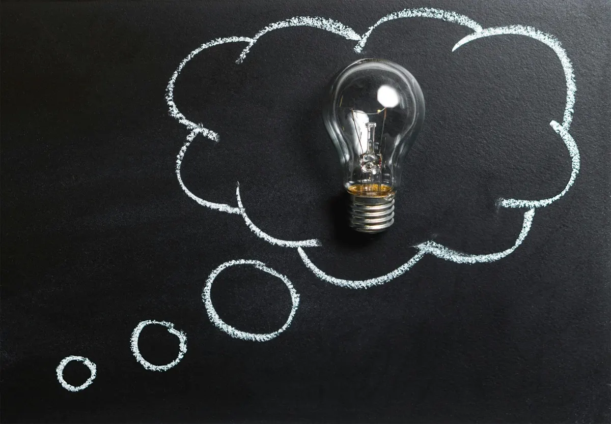 A light bulb inside a thought bubble drawn with chalk on a blackboard, symbolizing an idea or innovation.