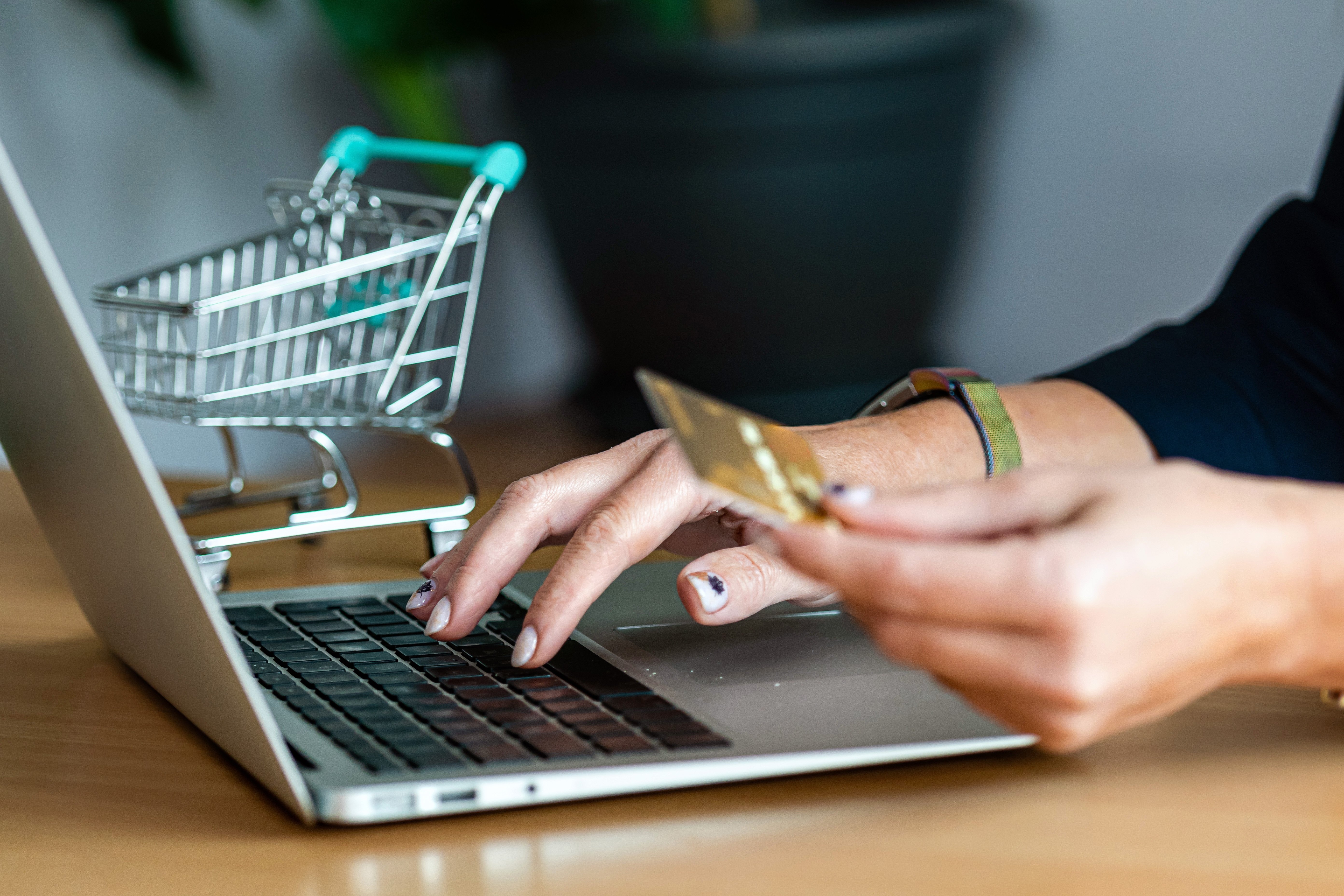 Person making an online purchase on their laptop and a shopping cart is seen in the background. 