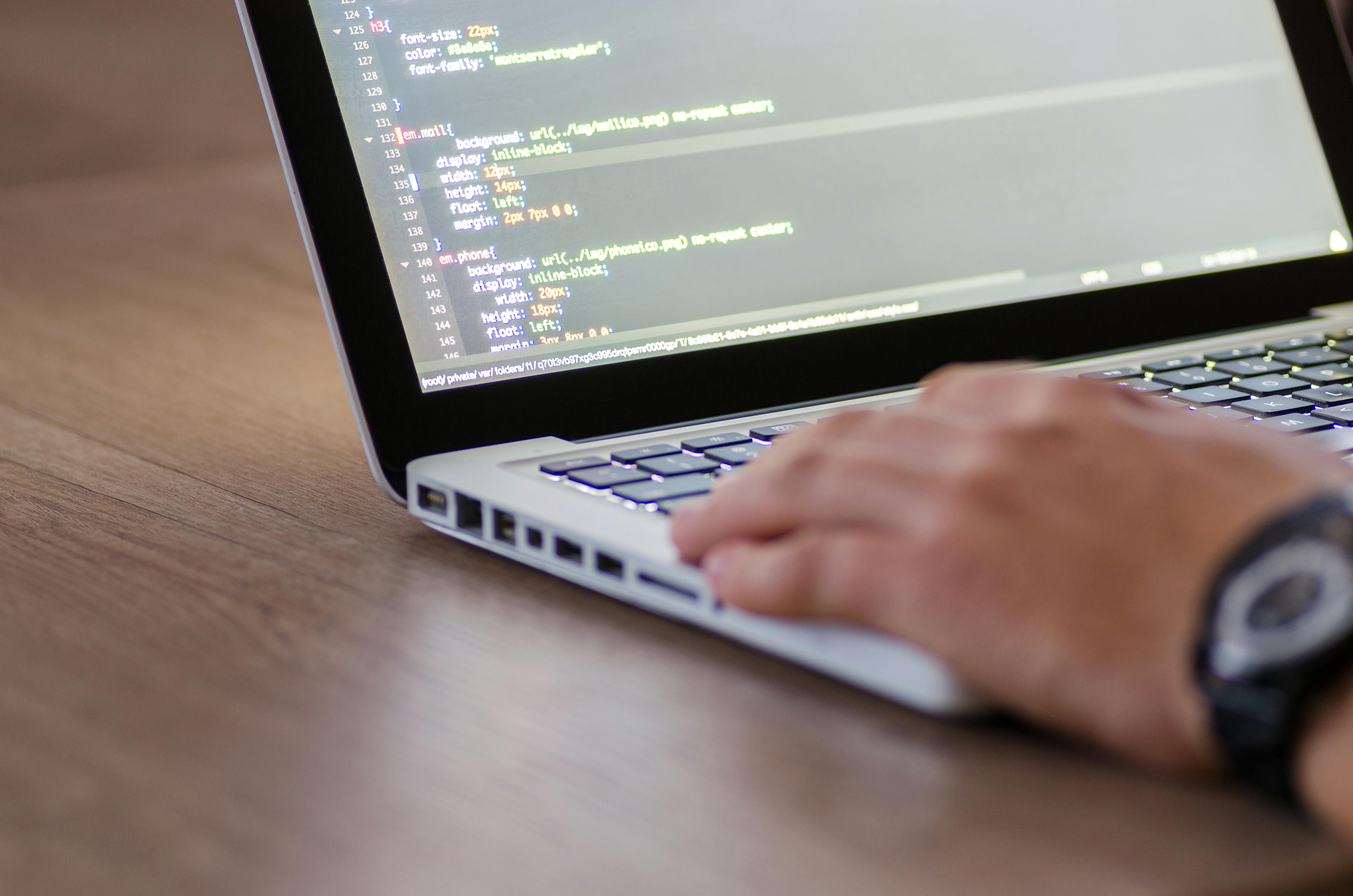 Close-up of a hand typing on a laptop keyboard with code displayed on the screen.